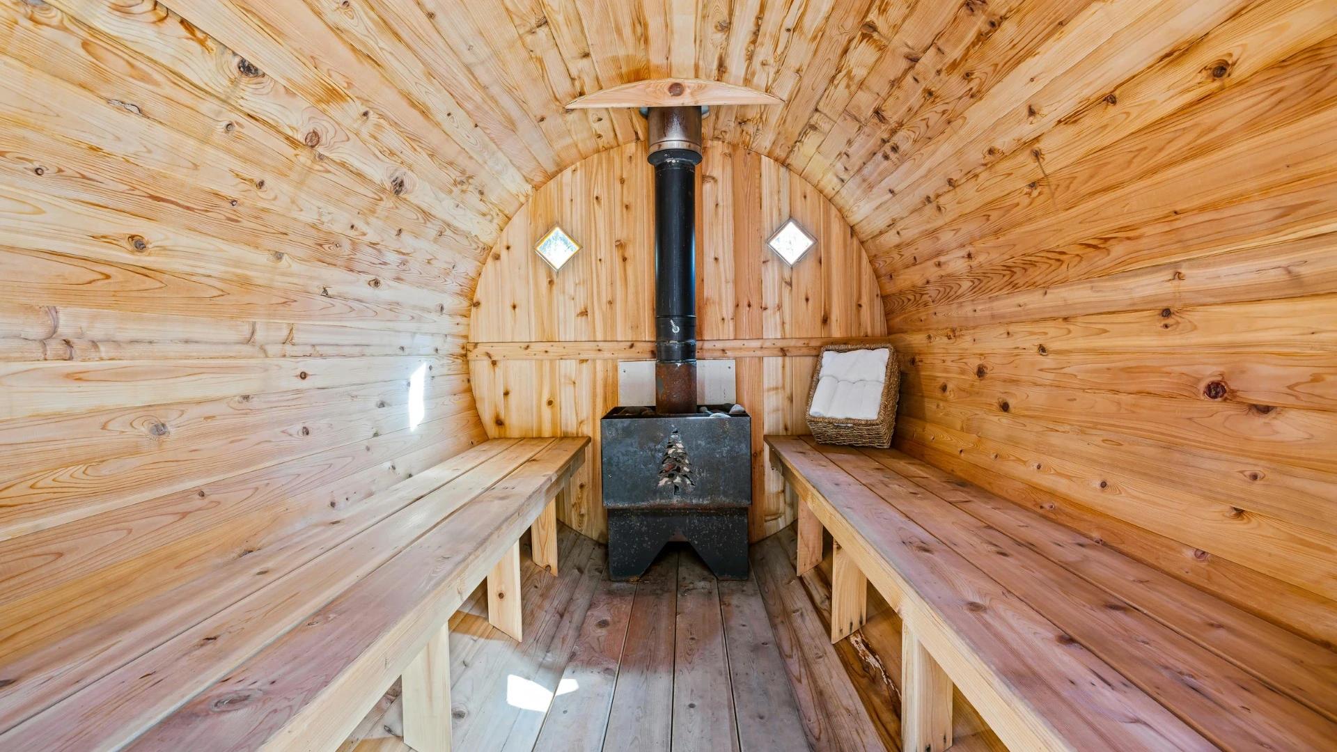 Inside a wood-fired barrel sauna: cedar benches either side of a black wood stove